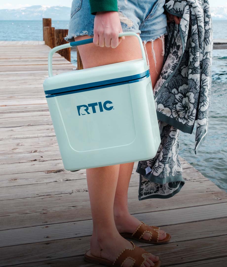 A person holding a small teal hard cooler on a dock.