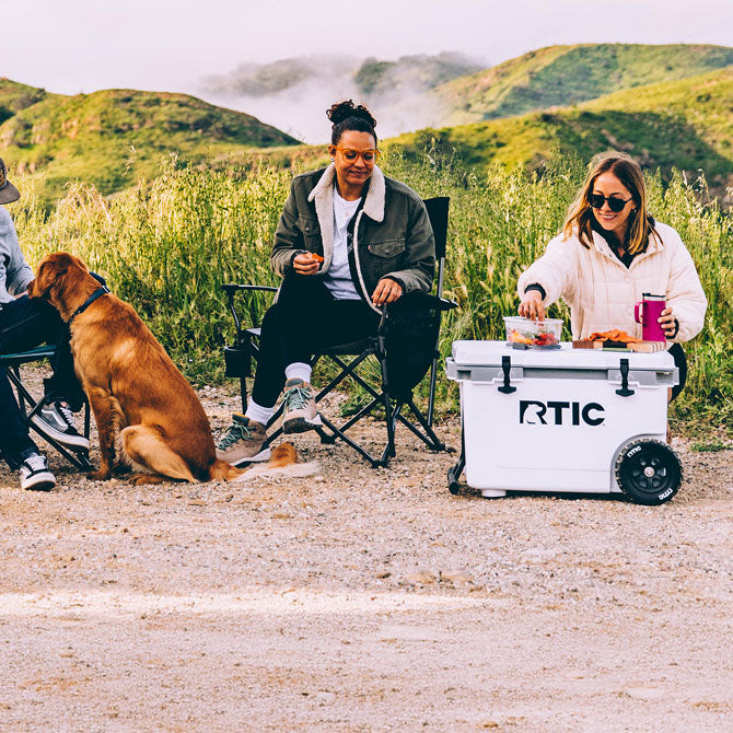 A group of friends camping with a white RTIC wheeled cooler.