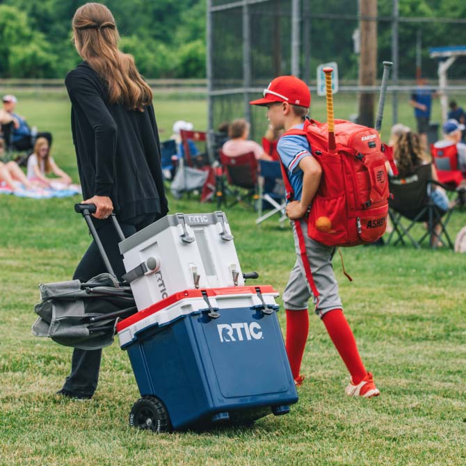 A family pulling a white RTIC wheeled cooler to the baseball field.